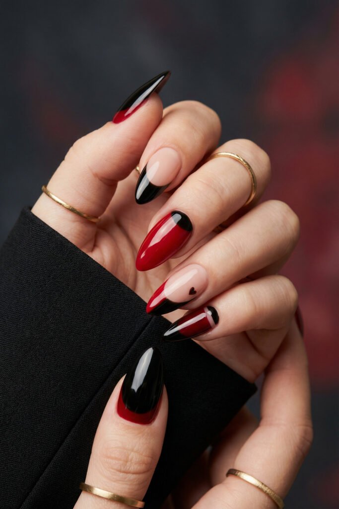 Black and Red Nails for a Bold, Polished Look 1 Hand with gold rings showing glossy almond nails in red black and nude with French tip accents and a tiny heart on one nail
