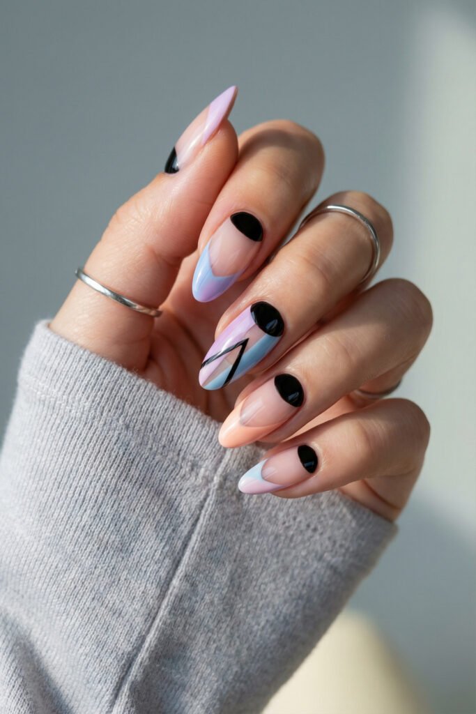 Pastel edgy spring nails with almond tips, black graphic accents, and soft blue, lilac, and blush color blocking on a sheer nude base.
