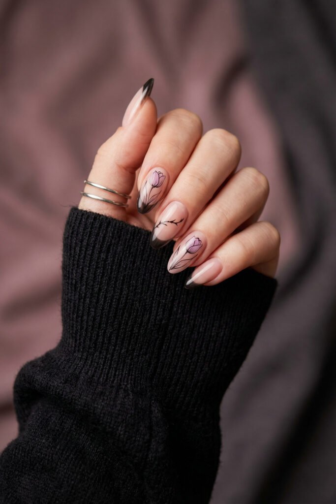Glossy almond nails with black gradient tips, lilac tulip art, and a minimalist branch detail for a romantic spring goth nails manicure with soft contrast.
