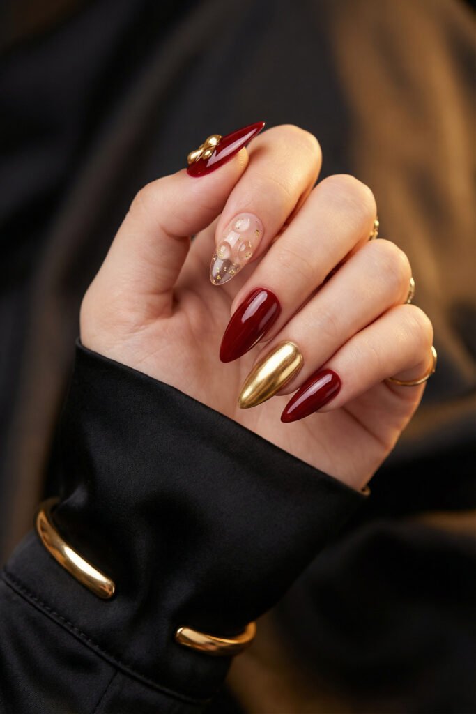 Chic Gold and Red Nails for a Bold, Polished Look 20 Hand with deep red almond nails featuring a mirror gold accent nail and a sheer nude accent nail with raised bubble art and gold flecks