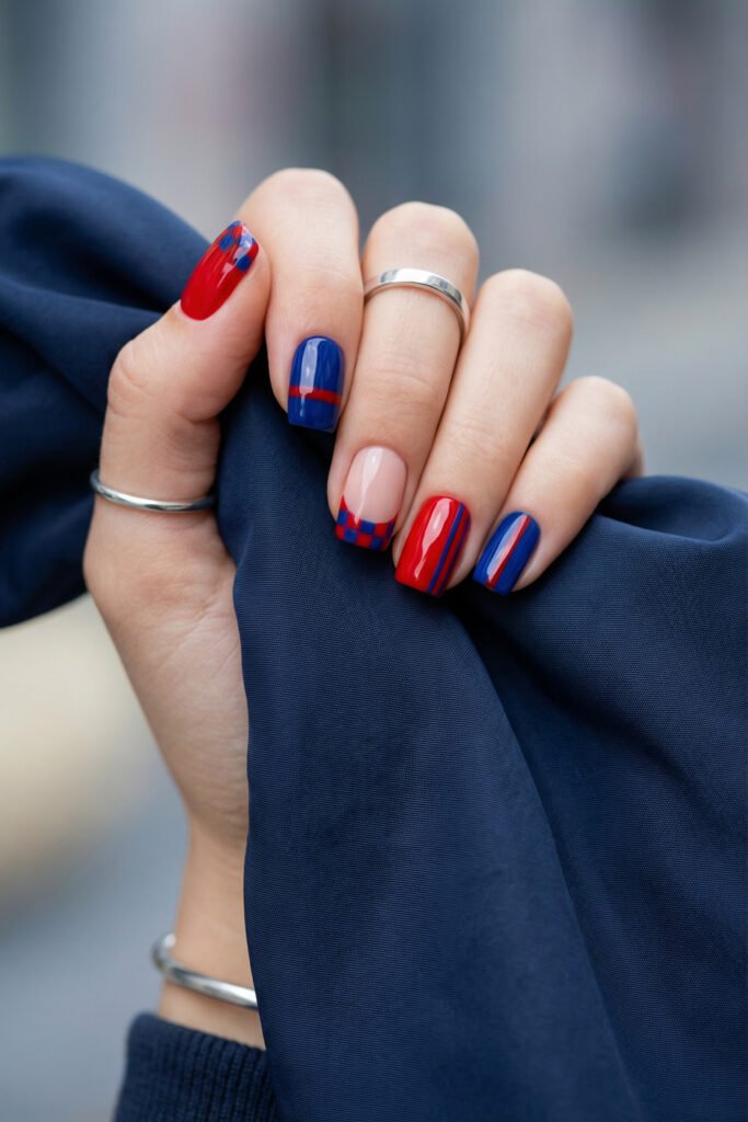Glossy blue and red nails with checkerboard French detail, sleek stripes, and solid color accents on short square nails holding blue fabric

