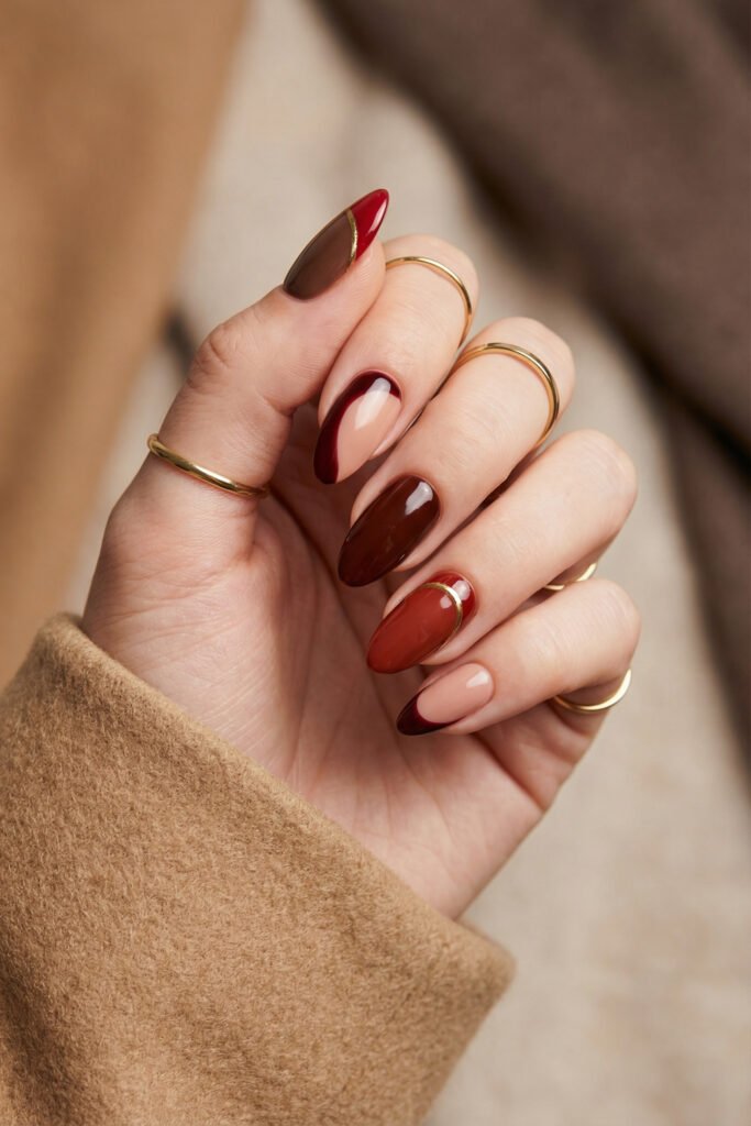 Elegant fall red nails in burgundy and brown with glossy finishes, nude accents, curved French details, and delicate gold outlining.
