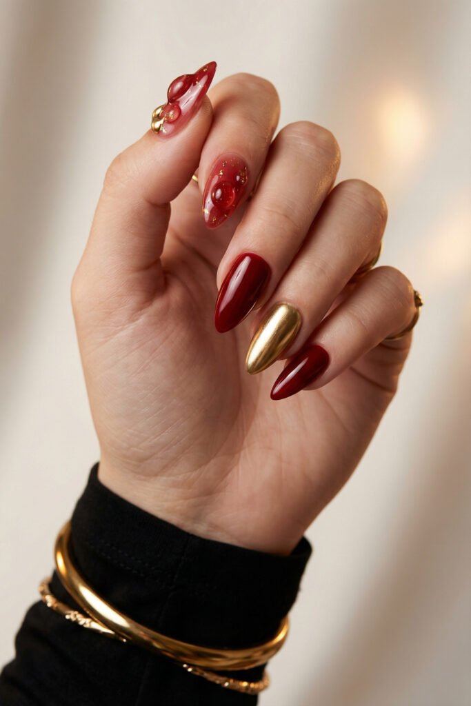 Chic Gold and Red Nails for a Bold, Polished Look 21 Close up of a hand with glossy red almond nails featuring a gold chrome accent nail and translucent bubble art nails with tiny gold flecks