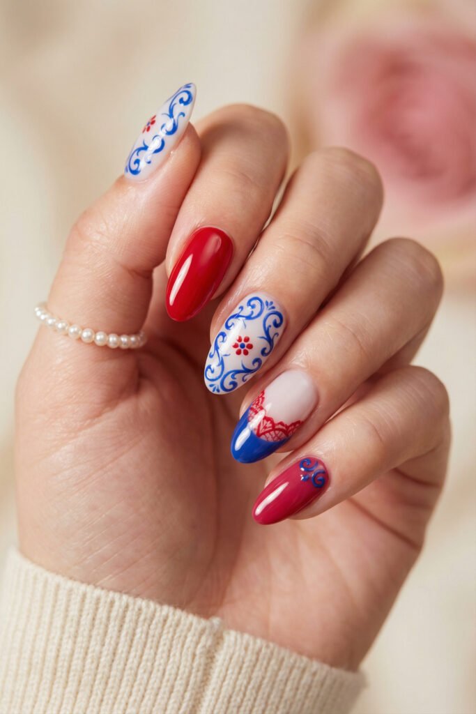 Almond blue and red nails with delicate folk-inspired scrollwork, floral details, and a blue French accent for an elegant artistic manicure
