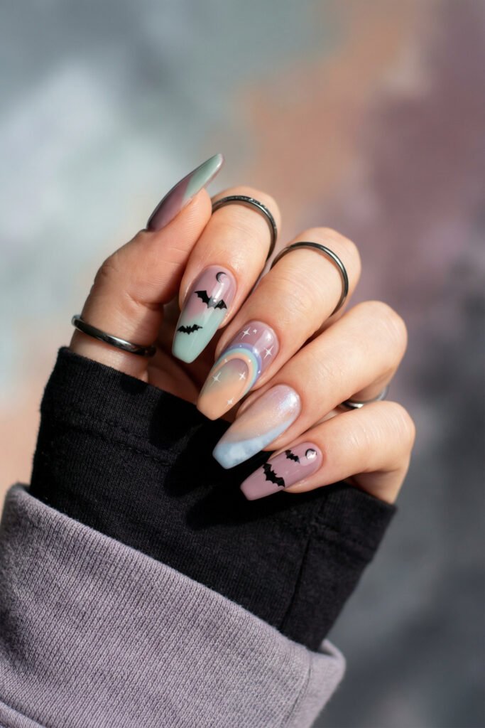 Pastel coffin nails with mint and lavender gradients, black bats, a rainbow accent, and celestial details for dreamy spring goth nails.
