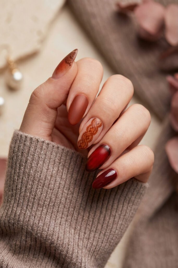 Elegant fall red nails in warm cinnamon and burgundy with lace accent art, a smoky red-black aura nail, and soft matte finishes.
