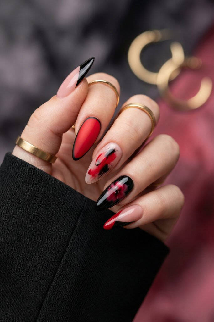Black and Red Nails for a Bold, Polished Look 24 Hand with gold rings showing almond nails in black red and nude with matte red polish floral blur art and abstract brushstrokes