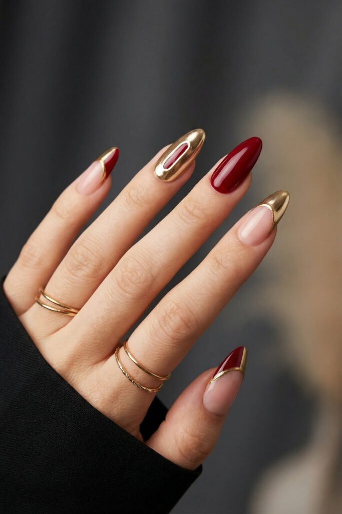 Chic Gold and Red Nails for a Bold, Polished Look 27 Close up of a hand with glossy red and nude almond nails featuring sculpted gold chrome details and one mirror gold accent nail against a dark backdrop