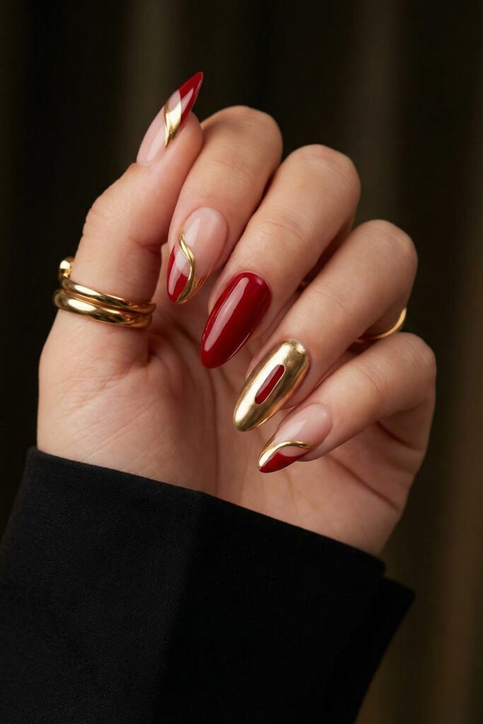 Chic Gold and Red Nails for a Bold, Polished Look 28 Hand with red and nude almond nails featuring sweeping gold chrome waves and a mirror gold accent nail with gold rings and a black sleeve