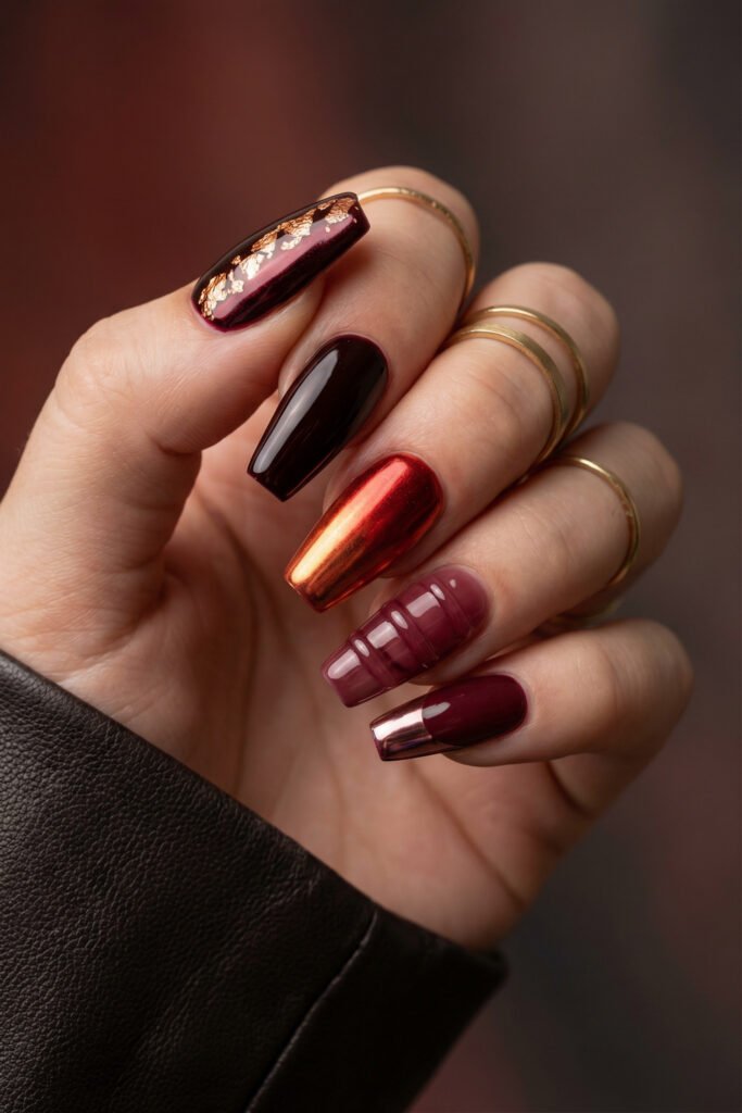 Long coffin fall red nails with deep burgundy gloss, copper chrome, gold foil, mauve jelly striping, and a metallic French tip.
