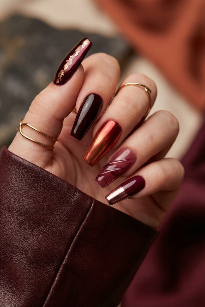 Dramatic fall red nails with black cherry gloss, molten copper chrome, plum jelly linework, gold foil, and a metallic tip detail.
