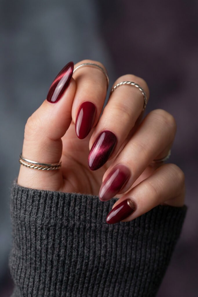 Glossy fall red nails with burgundy cat-eye shimmer, a red aura accent, and a bronze detail on almond-shaped nails.

