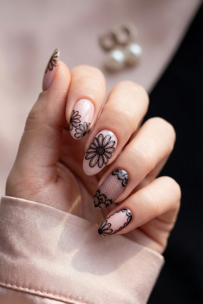 Soft pink almond nails featuring black floral lace outlines and a fishnet accent, styled as a delicate yet dramatic spring goth nails design.
