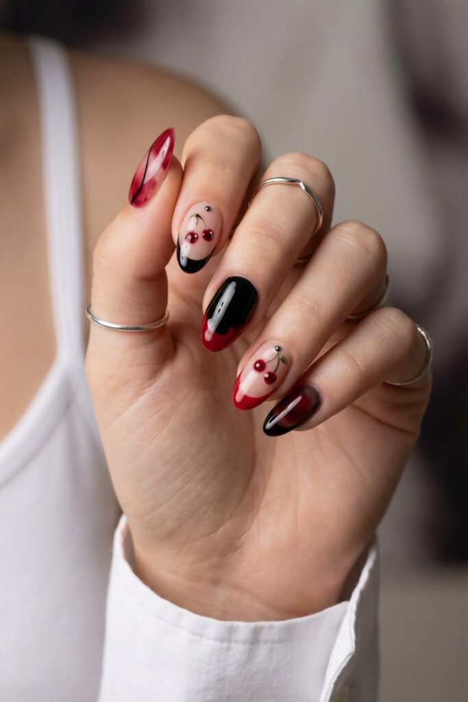 Black and Red Nails for a Bold, Polished Look 5 Hand with silver rings showing red black and nude almond nails featuring cherry art and glossy gradients against a soft indoor background