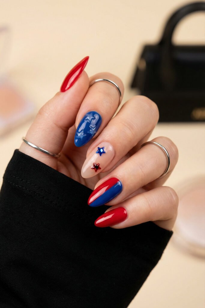 Glossy almond blue and red nails with 3D star details, sheer nude accent nail, red and cobalt polish, and silver rings
