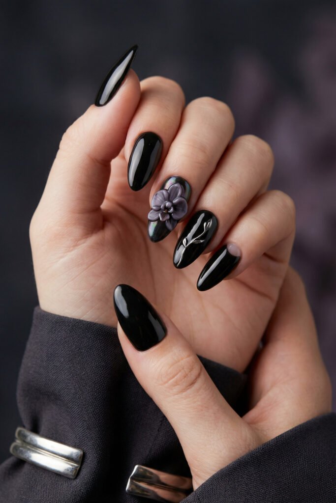 Glossy black almond nails with a sculpted lavender flower accent and subtle chrome detail, giving spring goth nails a bold, luxe, dark-romance finish.
