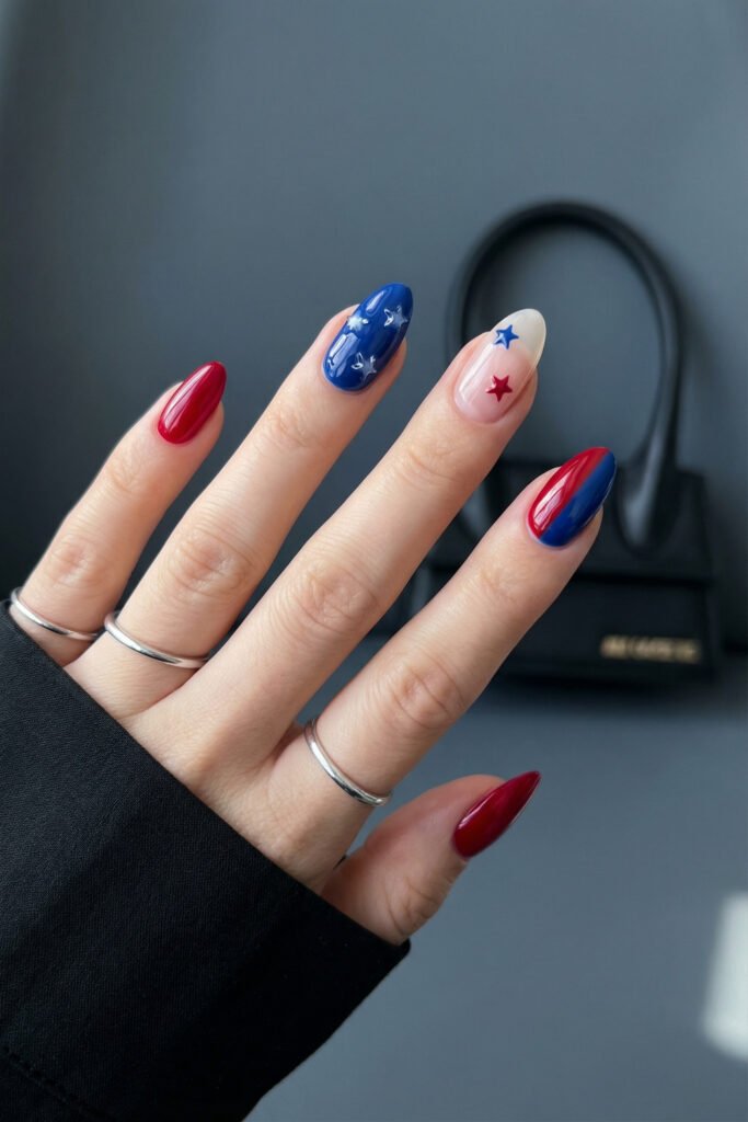 Full-hand view of blue and red nails with glossy almond shape, star accents, a nude feature nail, and a split red-blue design
