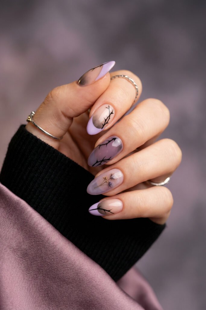 Lilac edgy spring nails with smoky gradients, black botanical linework, and tiny dried floral details on glossy almond nails.
