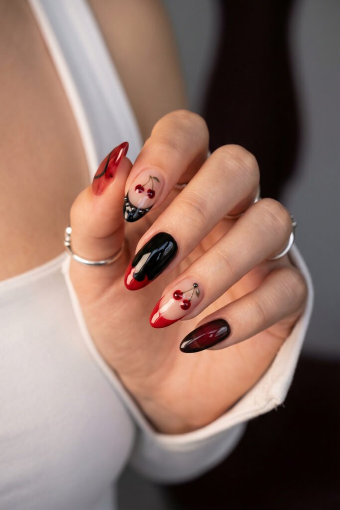 Black and Red Nails for a Bold, Polished Look 7 Hand with silver rings showing glossy almond nails in black red and nude featuring cherry art and a beaded accent on one French tip