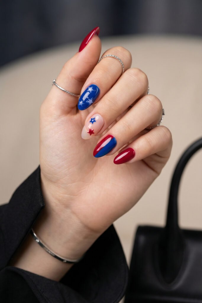 Elegant almond blue and red nails with raised star art, sheer nude accent, glossy color blocking, and a black blazer sleeve
