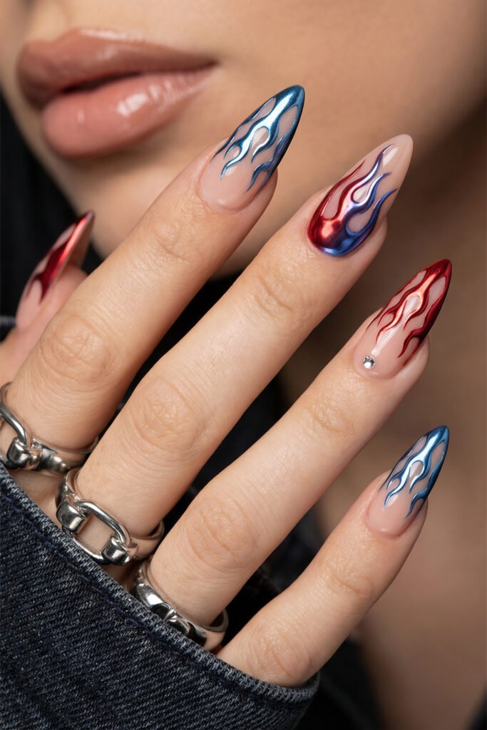 Long almond nude nails with metallic blue and red chrome flames, one tiny crystal accent, and silver rings
