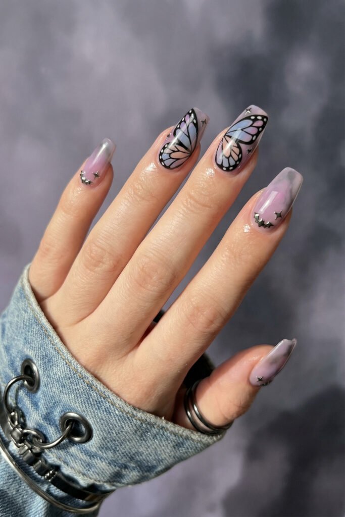 Coffin nails with butterfly wing art, smoky lilac marbling, and tiny silver star studs for an ethereal spring goth nails design with dreamy edge.
