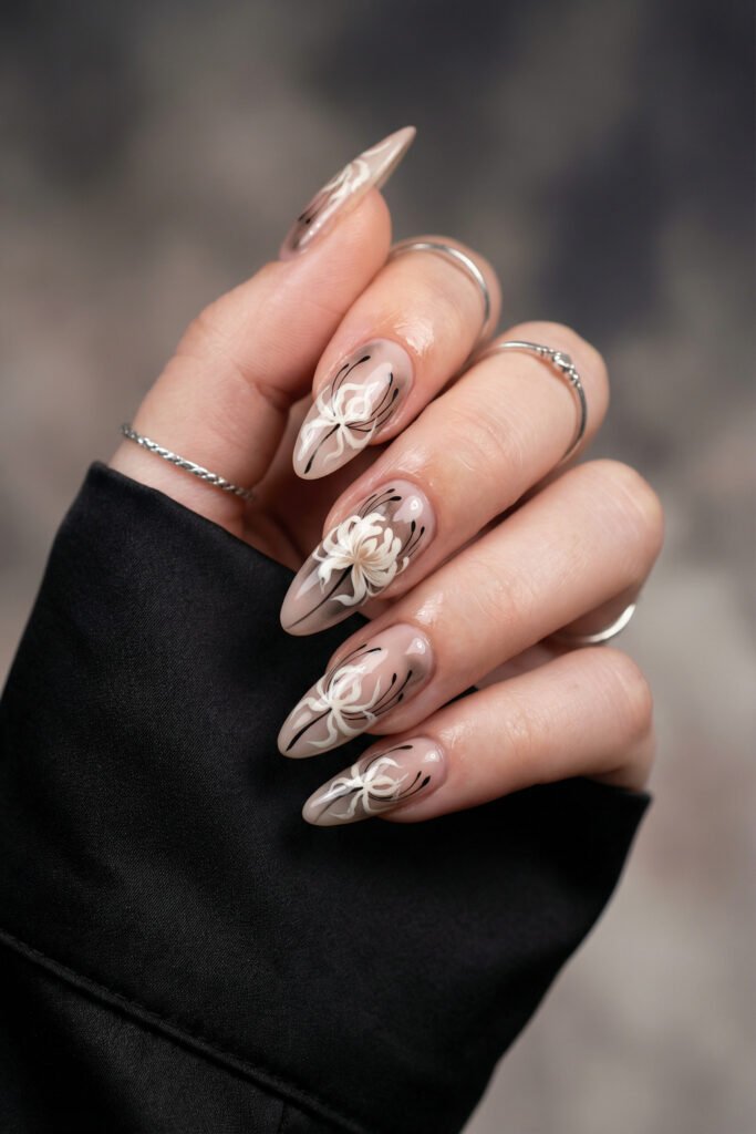 Nude almond nails with white spider lily-inspired flowers and fine black accents, a chic neutral spring goth nails look with soft gothic elegance.
