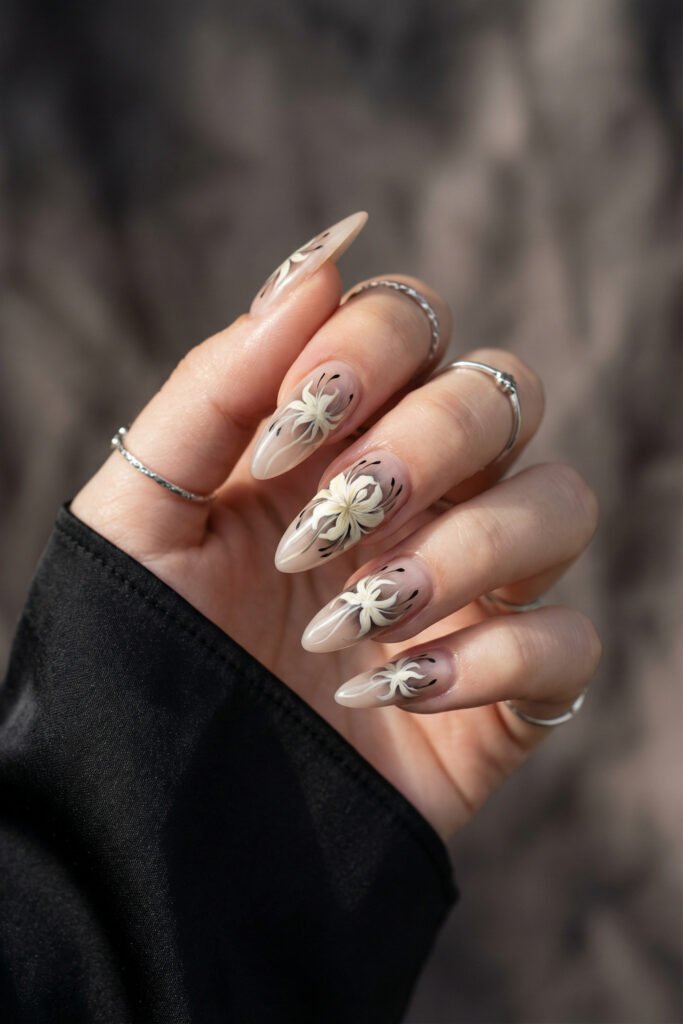 Neutral almond nails with creamy white floral art and delicate black detailing, capturing spring goth nails in a refined dark-romance manicure.
