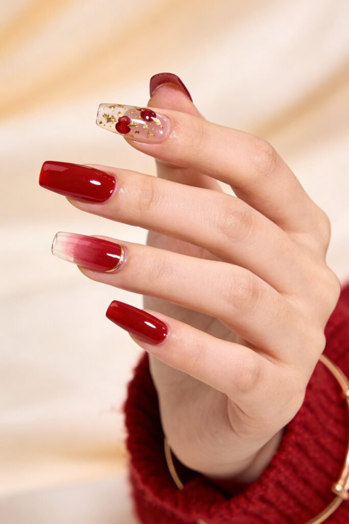 Chic Gold and Red Nails for a Bold, Polished Look 11 Hand with glossy red square nails featuring a clear accent nail with tiny red hearts and gold foil and a red ombre tip with a slim gold line