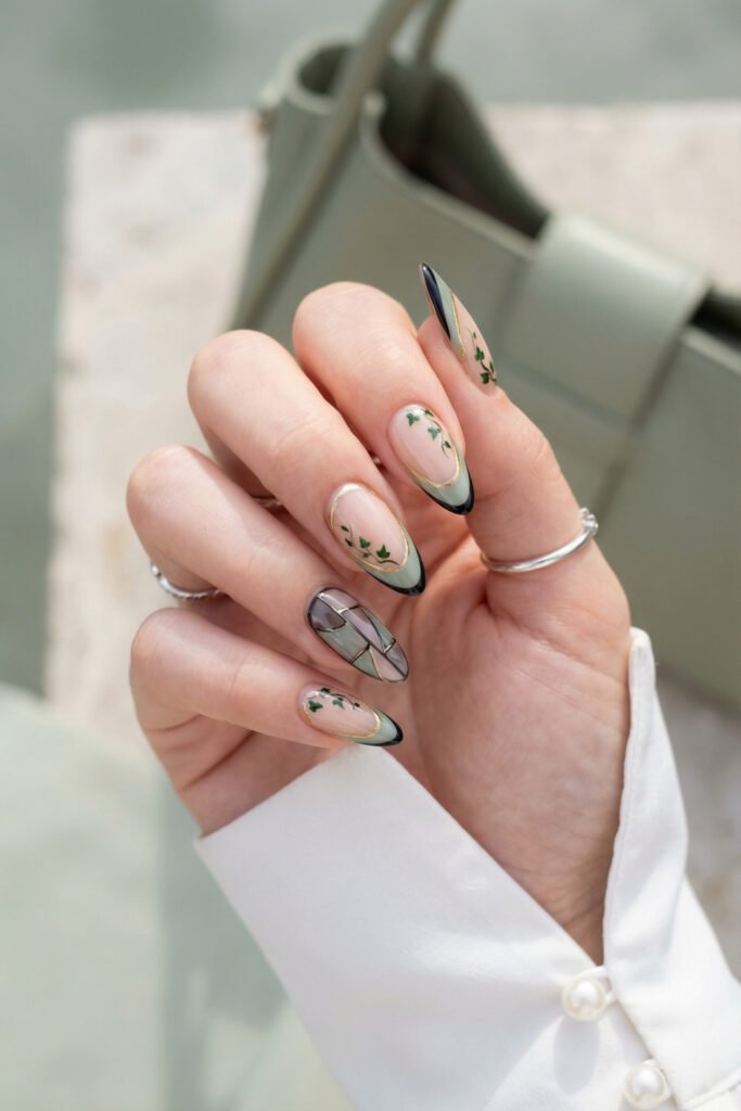 Sage and black almond French tips with gold outlines, tiny ivy accents, and a stained-glass detail nail for a refined botanical spring goth nails manicure.
