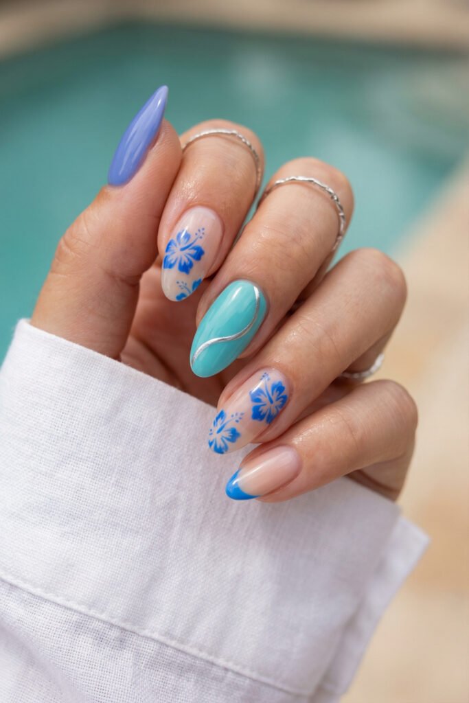 Spring Summer Nails That Feel Fresh and Easy 10 Blue tropical spring summer nails with hibiscus flower art, glossy aqua accent nail, silver wave detail, and a bright blue French tip by the pool.