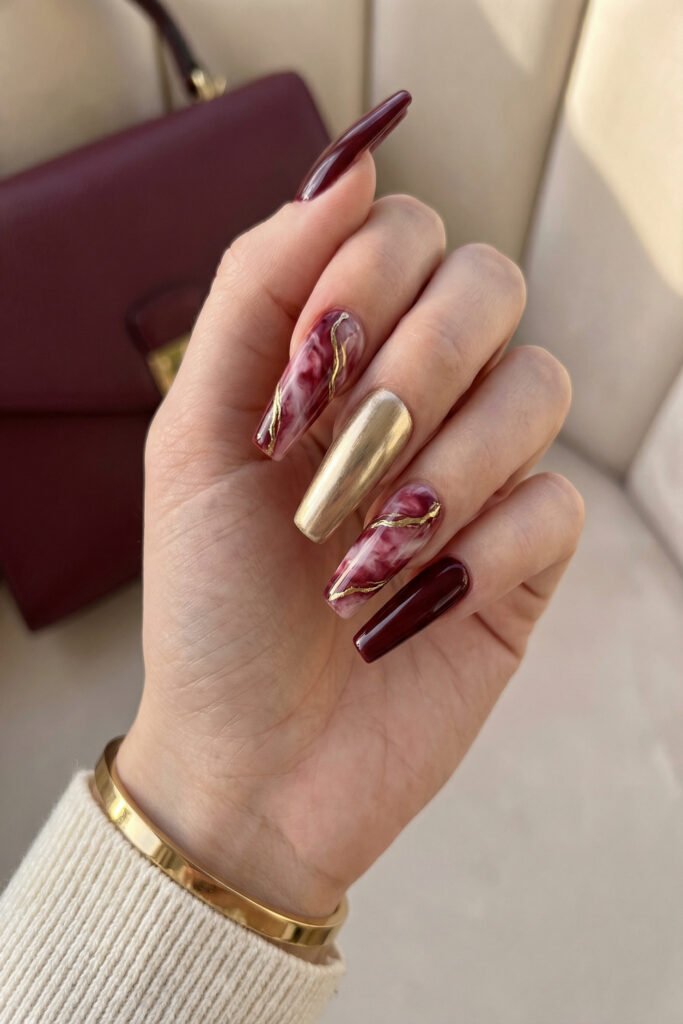 Chic Gold and Red Nails for a Bold, Polished Look 13 Hand with burgundy square nails featuring pink marbled accents and a brushed gold chrome nail with a cream knit sleeve and a burgundy bag