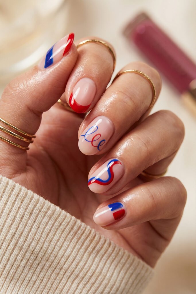 Short squoval blue and red nails on a sheer nude base with curved French tips, ribbon-like line art, and abstract color blocking in a glossy finish
