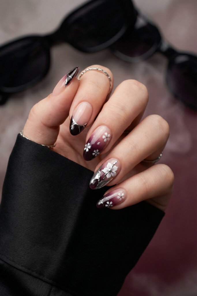 Deep plum edgy spring nails with white floral accents, silver metallic crack details, and glossy ombré almond shapes.
