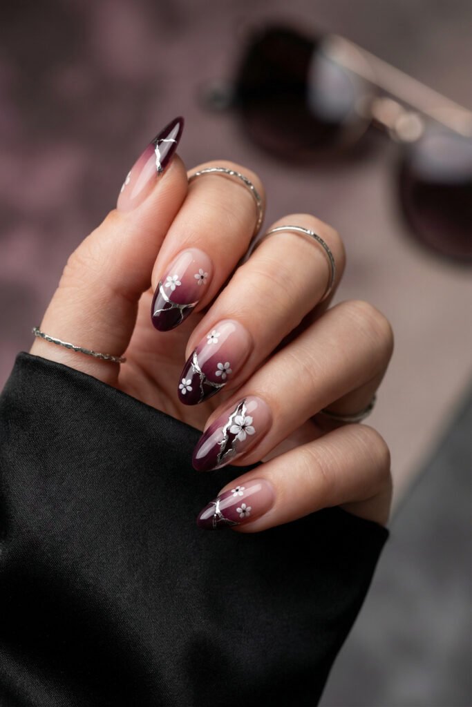 Berry-toned edgy spring nails with white flowers, silver chrome crack accents, and sheer nude almond nails.
