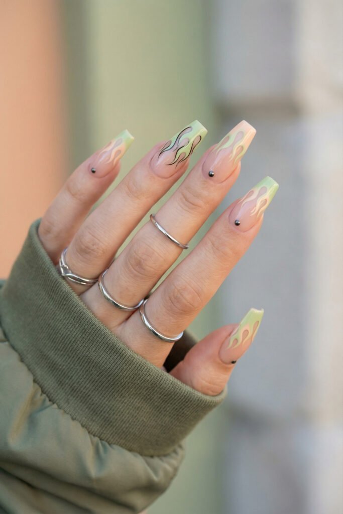 Sage and peach edgy spring nails with flame nail art, tiny metal studs, and long square nude nails.
