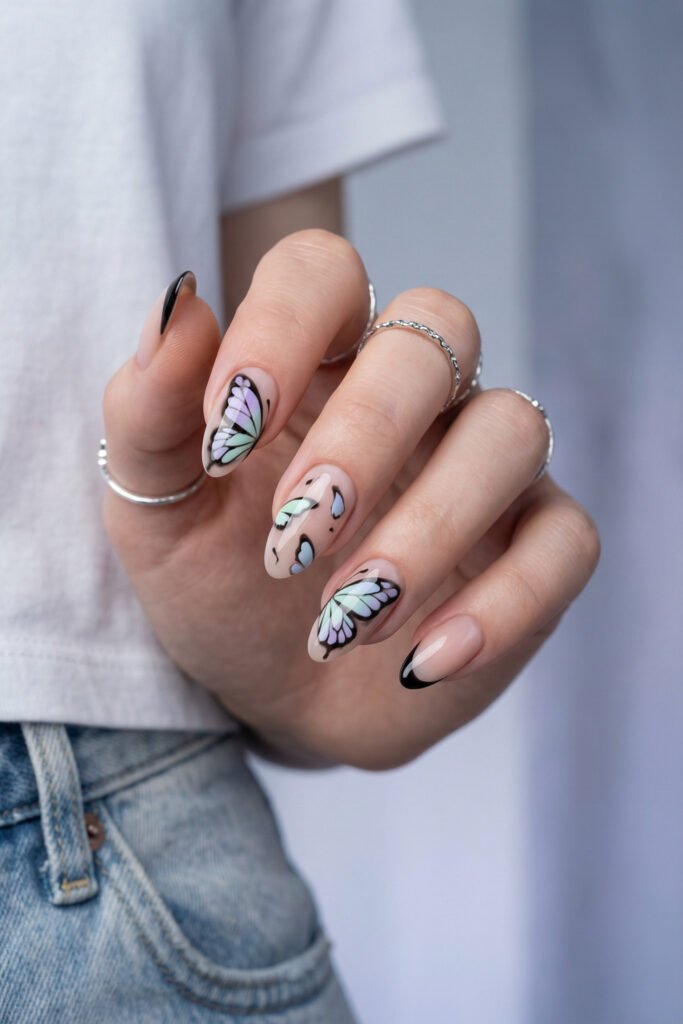 Pastel butterfly edgy spring nails with black outlines, soft lilac and mint wing details, and glossy nude almond nails.
