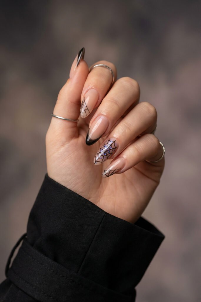 Glossy nude and black almond nails with delicate spider web designs and an iridescent web accent for a sleek spring goth nails look.
